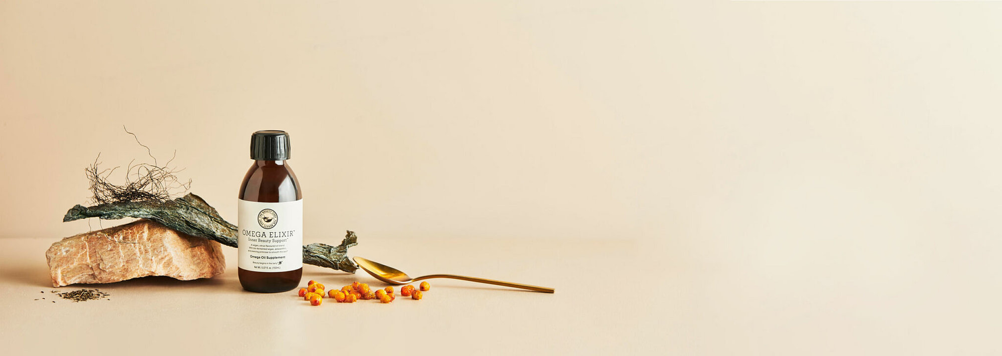 A photo of a styled amber bottle with seaweed, a rock and some berries. A good example of product photography Melbourne